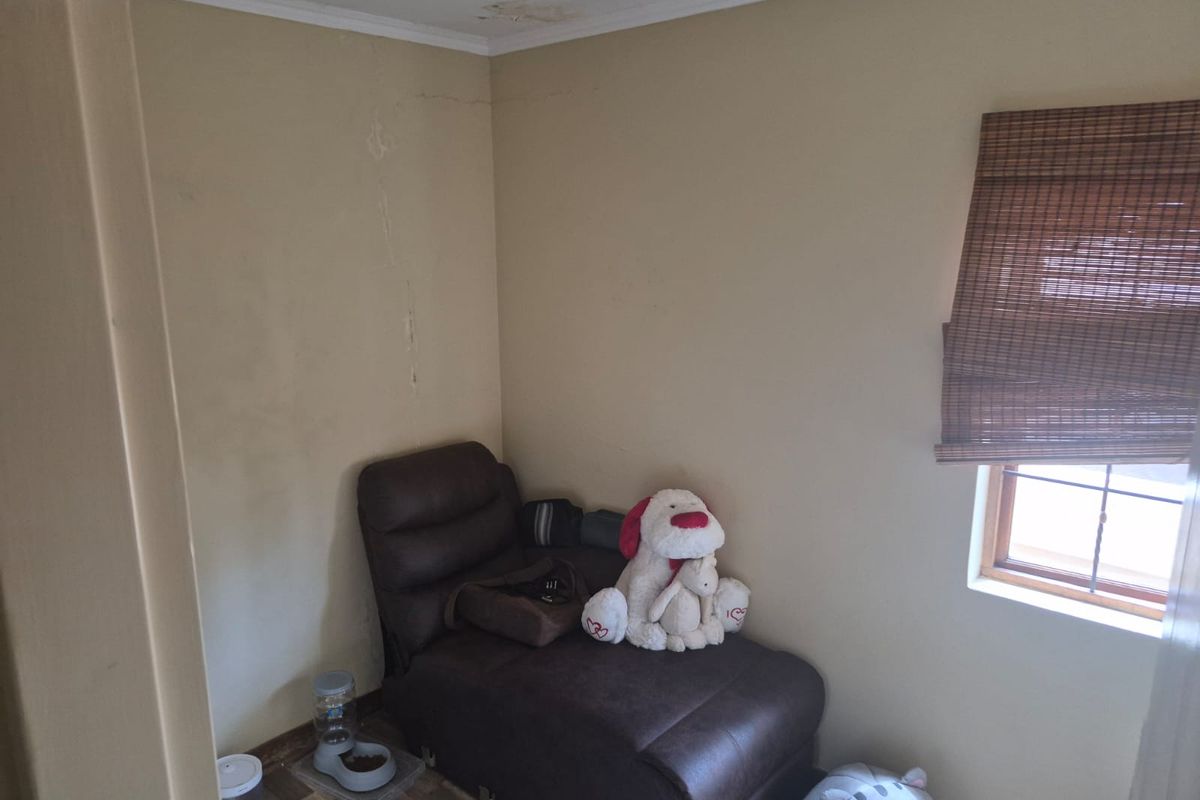 A small bedroom space featuring laminate flooring and a timber window with a bamboo blind, showing signs of ceiling water damage and wall cracking.