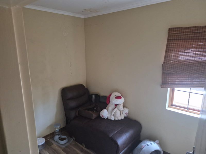 A small bedroom space featuring laminate flooring and a timber window with a bamboo blind, showing signs of ceiling water damage and wall cracking.