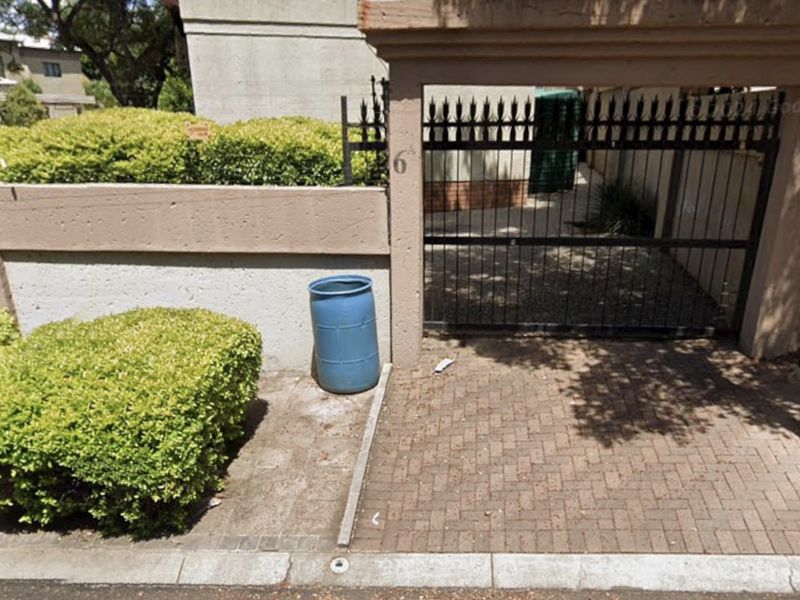 Front entrance view featuring a metal security gate, brick paved driveway, and concrete boundary wall with electric fencing.