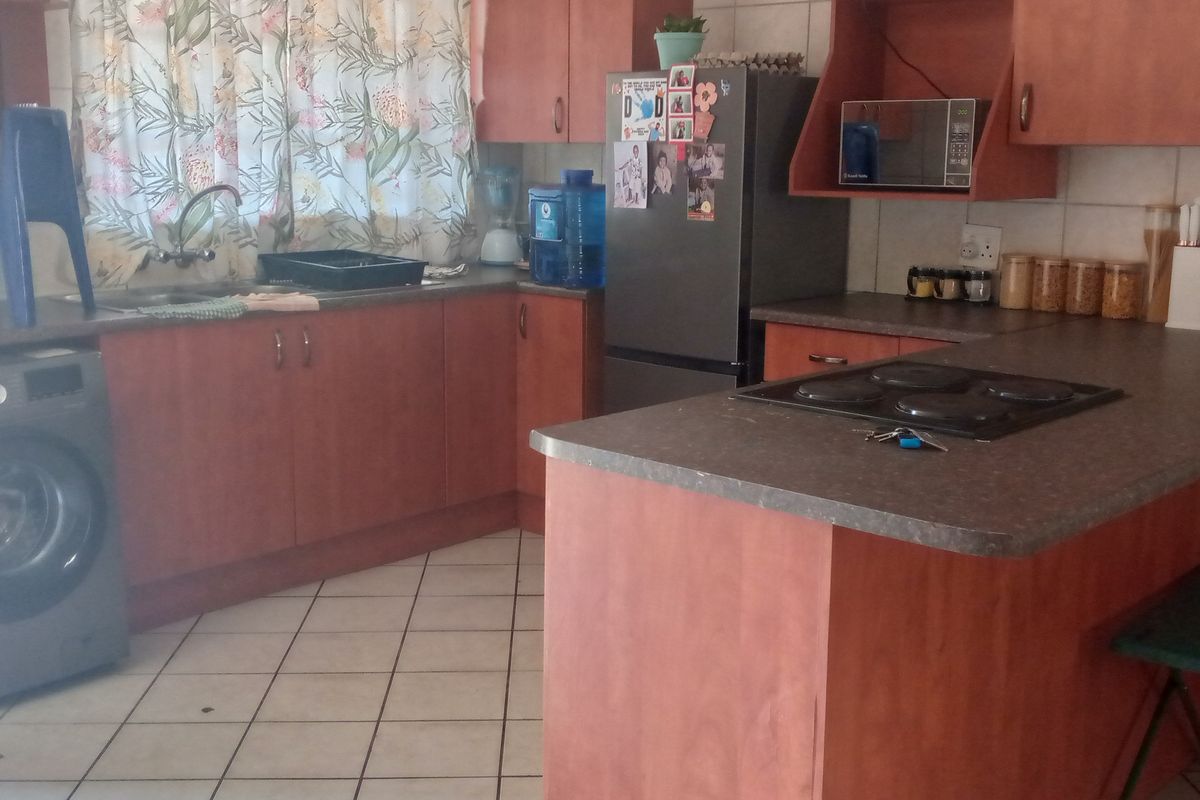 A functional kitchen featuring laminate cabinetry, tiled flooring, a built-in electric hob, and a double sink with a tiled backsplash.