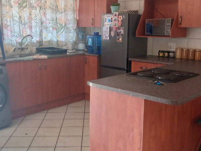 A functional kitchen featuring laminate cabinetry, tiled flooring, a built-in electric hob, and a double sink with a tiled backsplash.