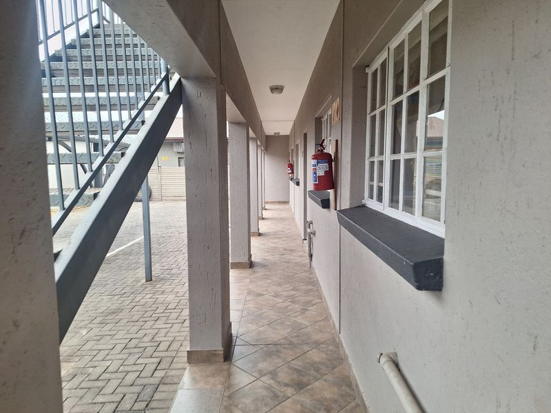 An exterior covered walkway featuring tiled flooring, metal staircase access, and wall-mounted fire safety equipment in a residential flat complex.
