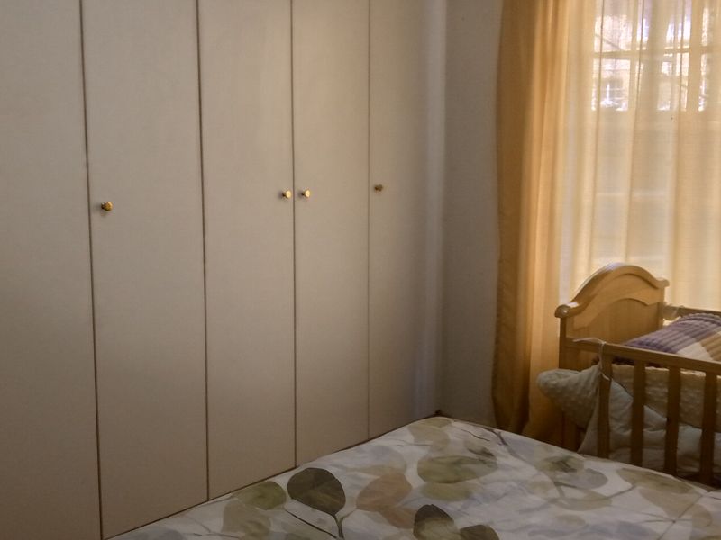 A bedroom featuring floor-to-ceiling built-in cupboards and natural light through a window with curtains.