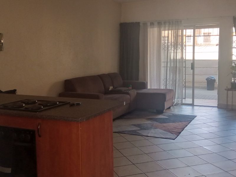 Open-plan living area featuring a kitchen with built-in cabinetry, hob, and oven, leading to a tiled lounge area with access to an outdoor patio.