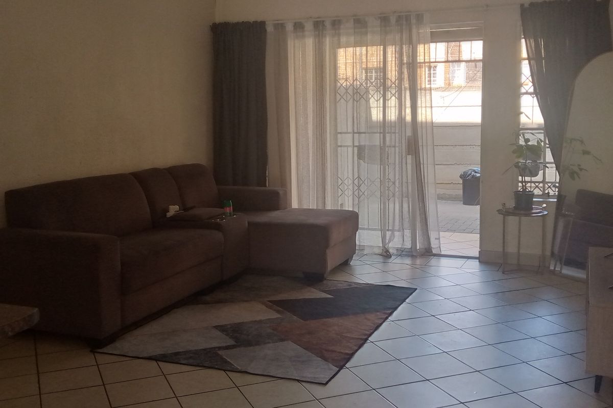 A living room featuring tiled flooring and a sliding glass door with a security gate, providing access to an outdoor area.