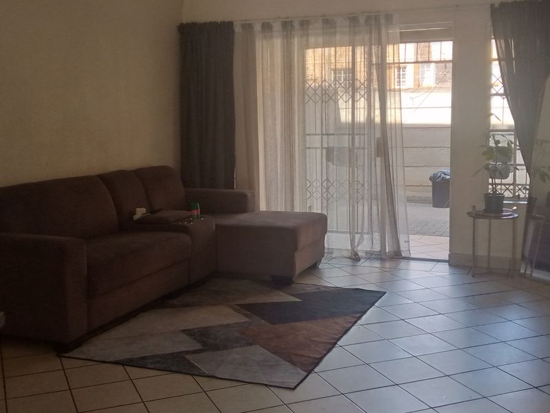 A living room featuring tiled flooring and a sliding glass door with a security gate, providing access to an outdoor area.