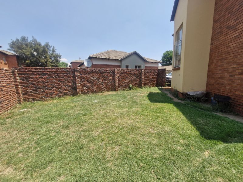 A private rear garden featuring a lawn area enclosed by a high brick boundary wall, adjacent to the townhouse's facebrick exterior.