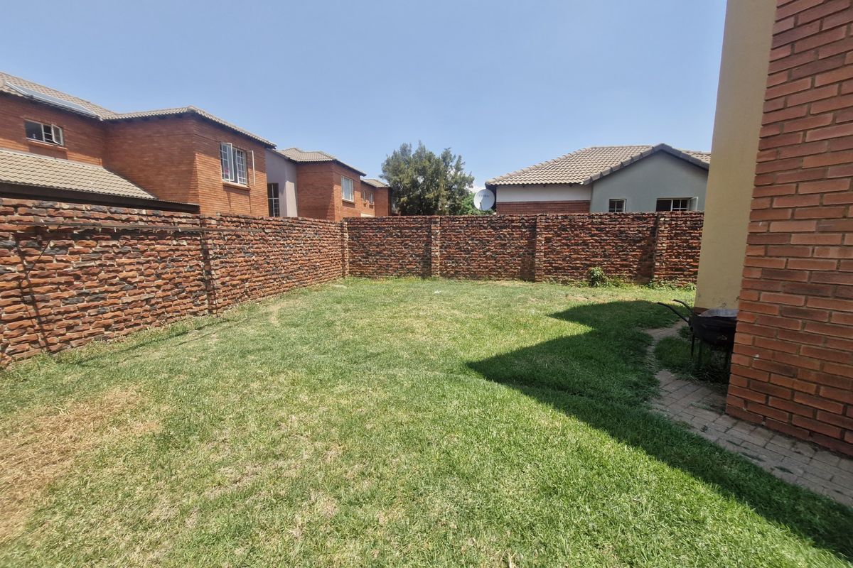 A private rear garden featuring a lawn area enclosed by a brick boundary wall and a paved walkway.