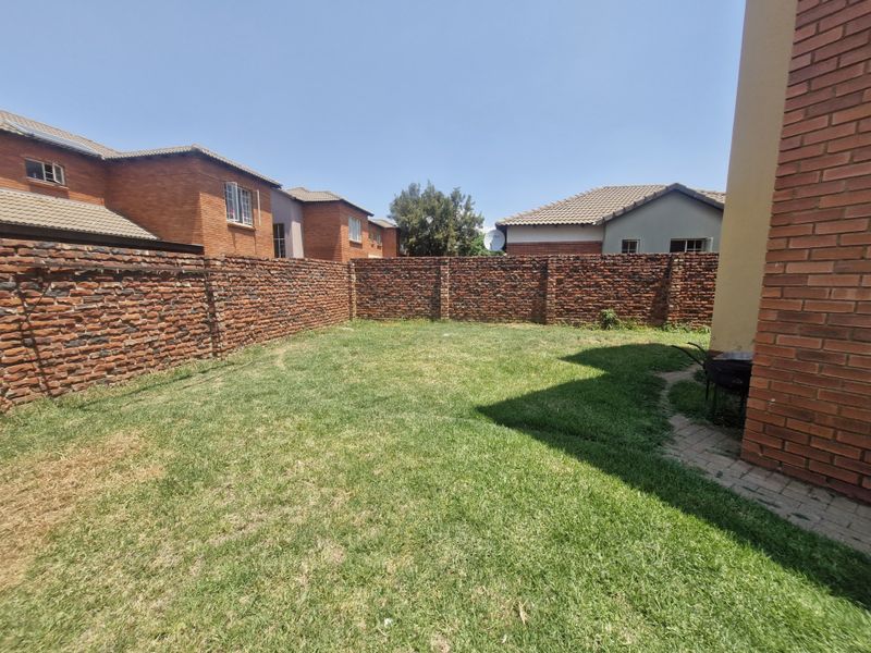 A private rear garden featuring a lawn area enclosed by a brick boundary wall and a paved walkway.