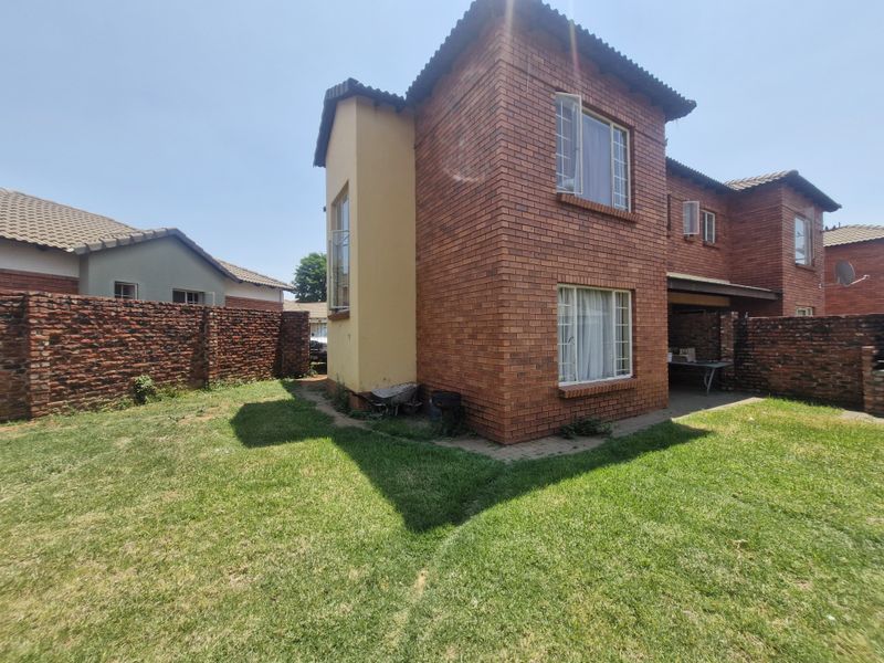 Rear view of a double-story face brick townhouse featuring a private garden, paved patio area, and perimeter brick walling.