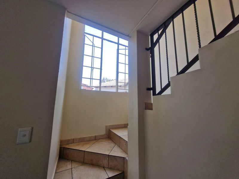 A bright staircase area featuring tiled steps, a metal balustrade, and a large window allowing natural light into the hallway.