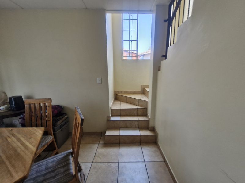 A functional hallway area featuring tiled flooring and a staircase with a metal balustrade, leading to an upper level with natural light.