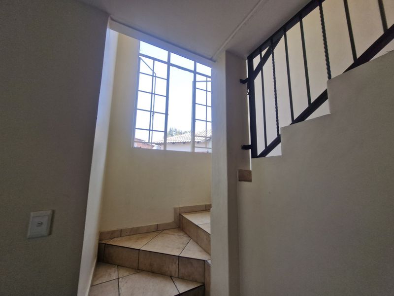A staircase area featuring tiled steps, a wrought iron balustrade, and a large steel-framed window allowing natural light into the hallway.