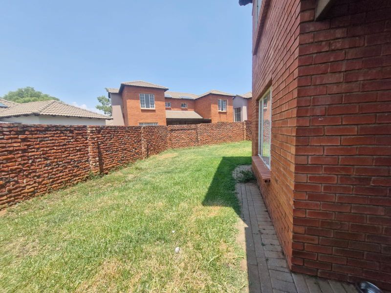A private rear garden area featuring a brick boundary wall, a paved walkway along the townhouse exterior, and a grass lawn.