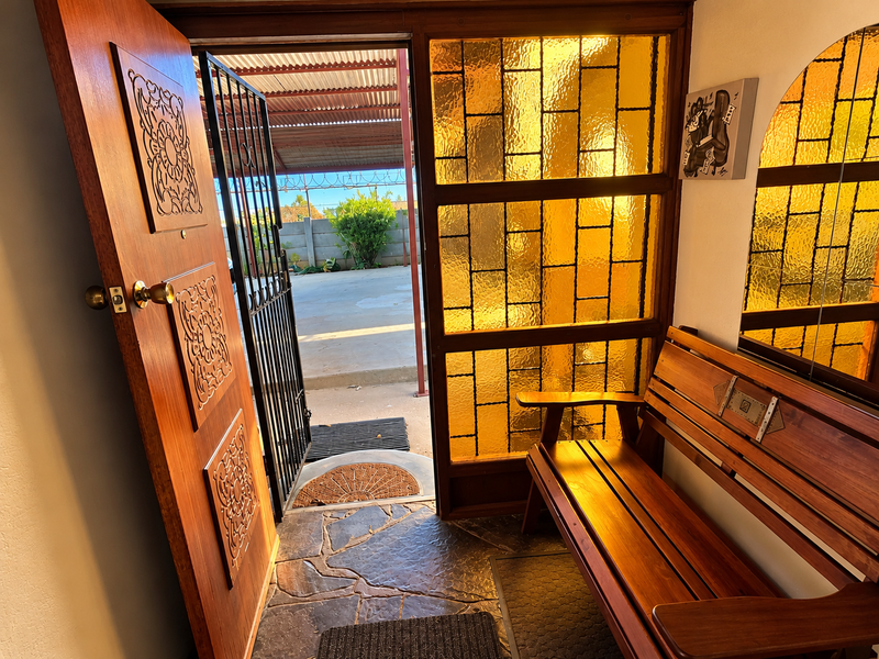 A welcoming entrance hall featuring a decorative carved wooden door, a security gate, and distinctive amber stained glass sidelights with natural flagstone flooring.