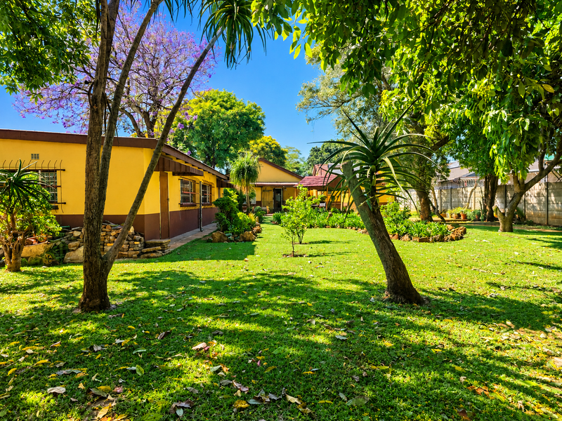 A spacious rear garden featuring a well-maintained lawn, mature trees, and a yellow-painted exterior facade with security-fitted windows.