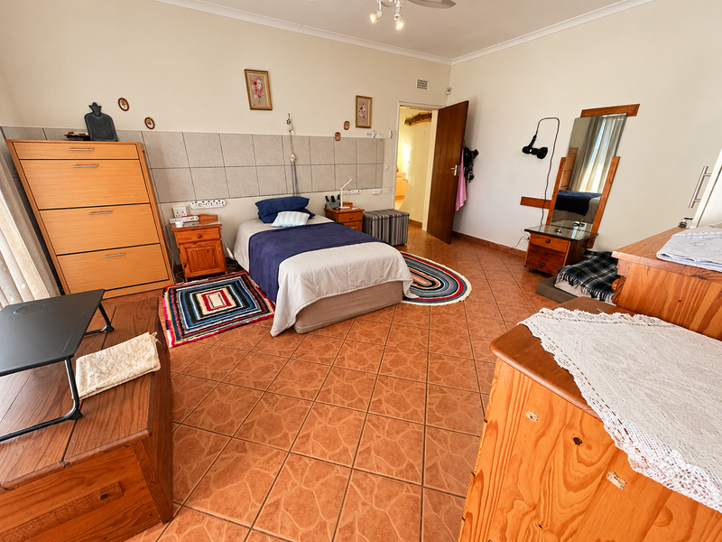 A spacious bedroom featuring tiled flooring, a tiled wall accent, and a ceiling fan, offering a functional layout with direct access to adjacent rooms.