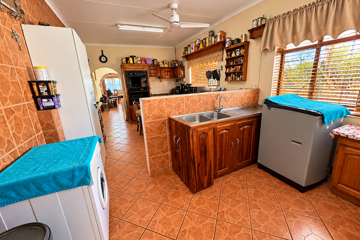 A functional kitchen featuring wooden cabinetry, tiled surfaces, a double sink, and a built-in oven, with an open-plan layout connecting to the living area.