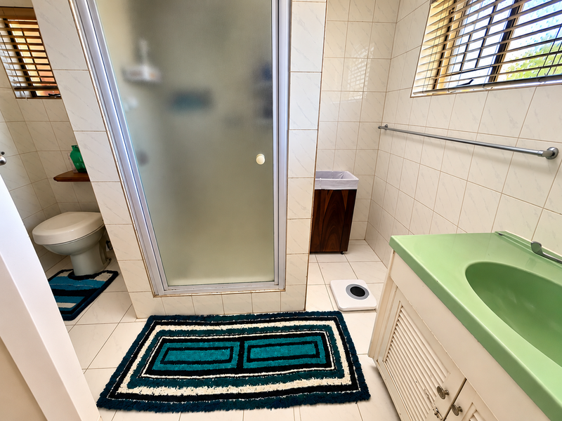 A functional bathroom featuring a shower enclosure, vanity with integrated sink, toilet, and neutral wall tiling.