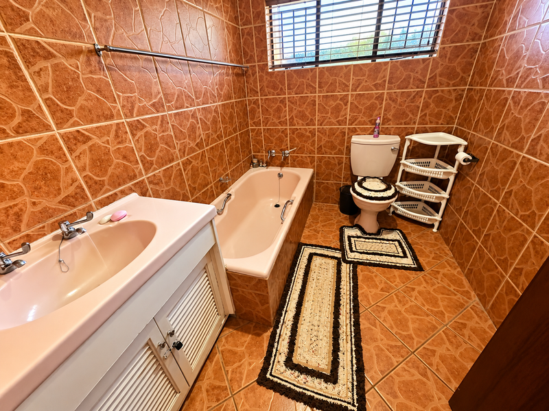 A functional bathroom featuring a built-in vanity, bathtub, and toilet, finished with full-height wall tiling and matching floor tiles.