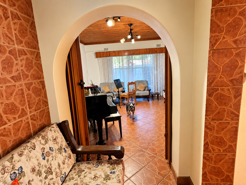 A view through an arched doorway into a living area featuring terracotta floor tiles and a timber-paneled ceiling.