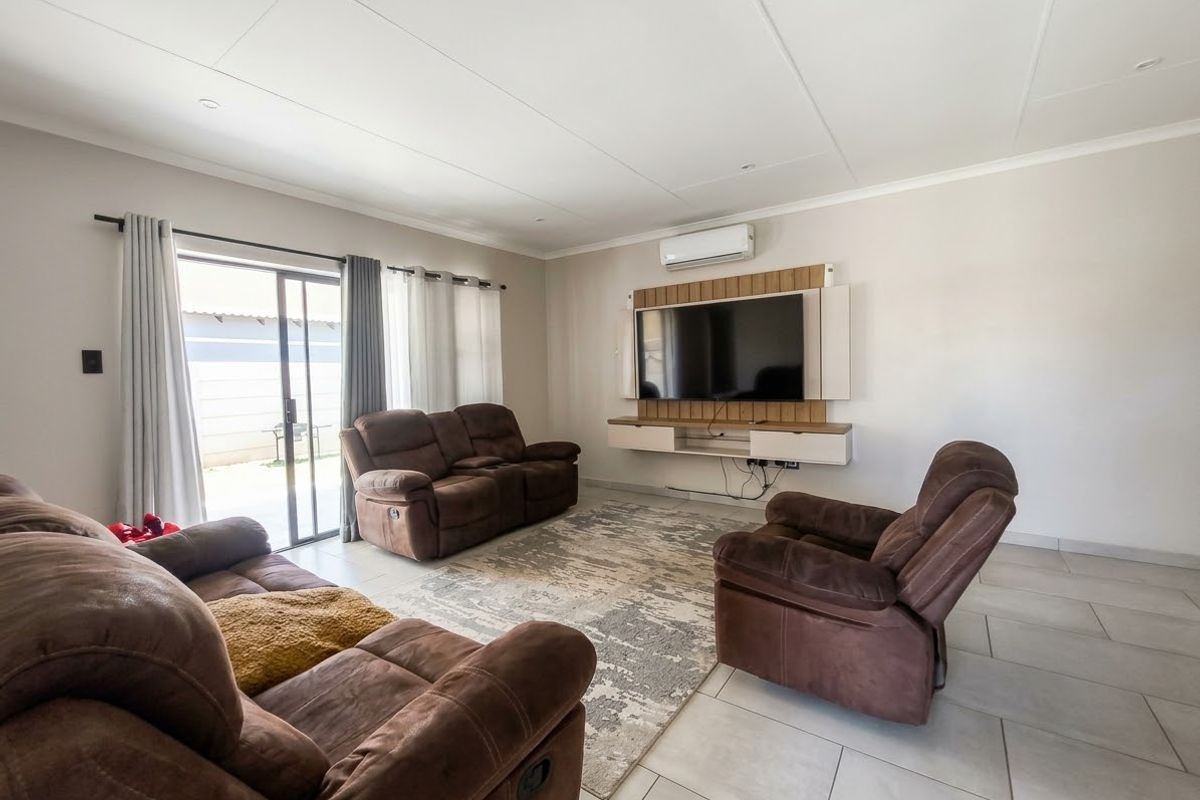A bright and spacious living room featuring tiled flooring, a wall-mounted air conditioning unit, and a modern built-in media console with sliding door access to the patio.