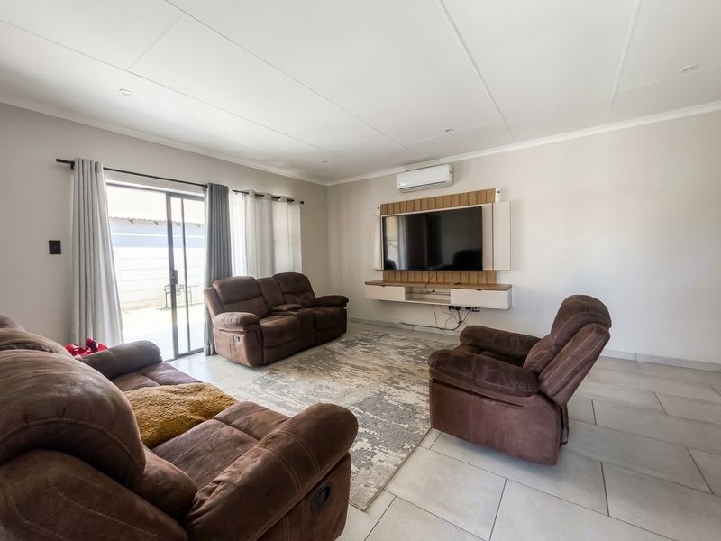 A bright and spacious living room featuring tiled flooring, a wall-mounted air conditioning unit, and a modern built-in media console with sliding door access to the patio.