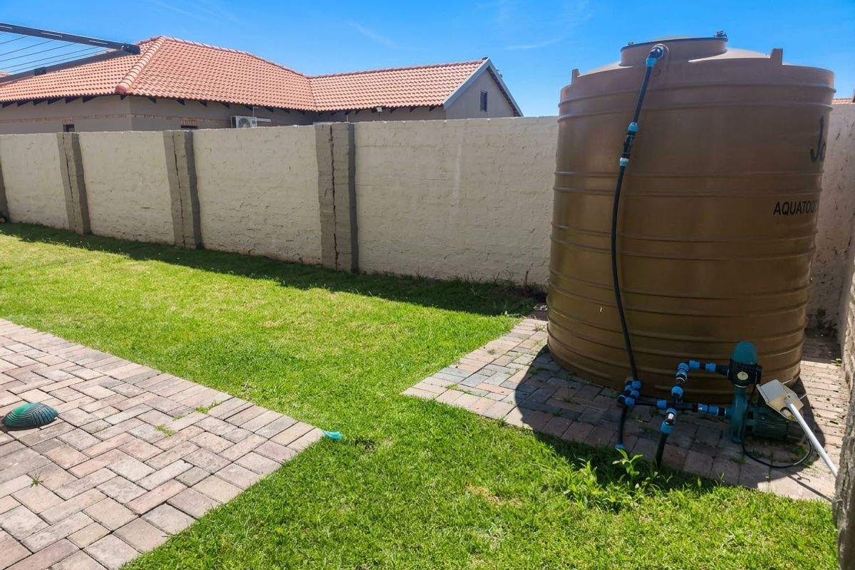 Rear garden area featuring a water storage tank with pump, paved section, and a perimeter boundary wall.