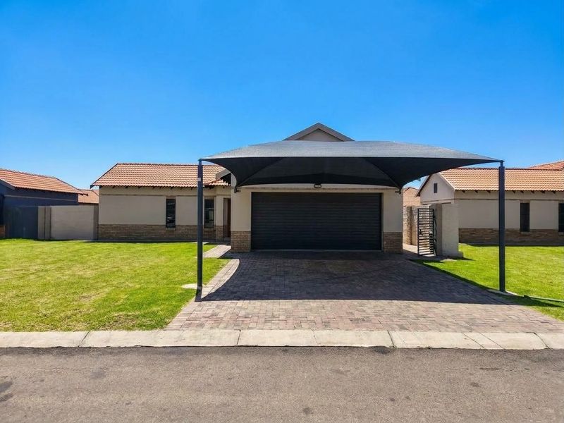 Front elevation of a townhouse featuring a paved driveway, a modern shade sail carport, and a secure garage entrance with well-maintained lawn.