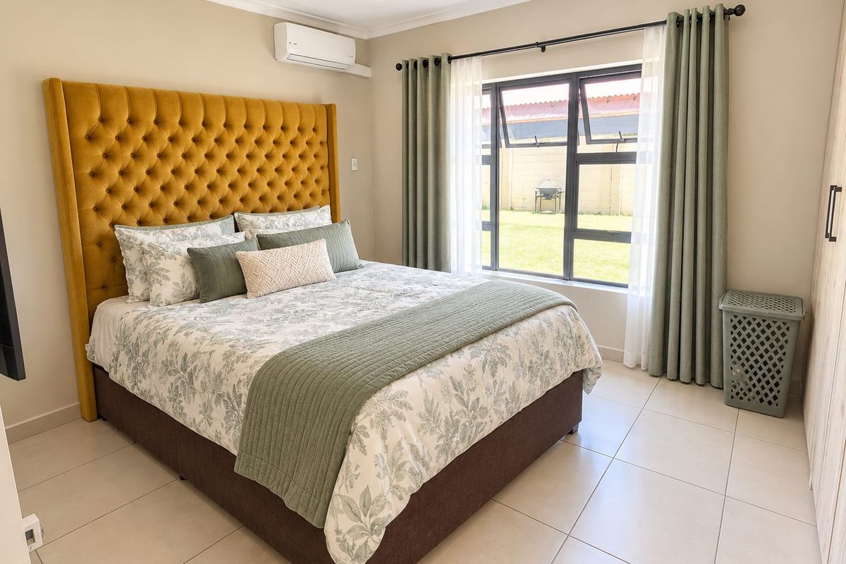 A well-maintained bedroom featuring tiled flooring, built-in cupboards, and an air conditioning unit, with large windows providing natural light.