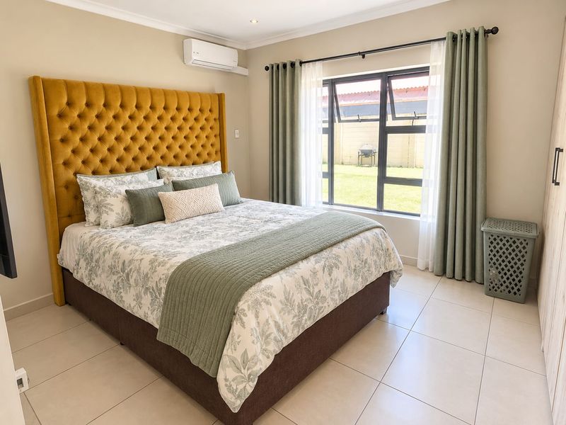 A well-maintained bedroom featuring tiled flooring, built-in cupboards, and an air conditioning unit, with large windows providing natural light.
