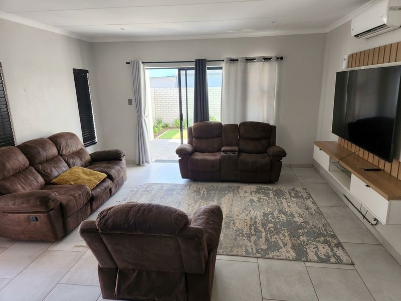 A bright and modern living room featuring tiled floors, a feature timber wall, and direct access to a private patio through sliding glass doors.