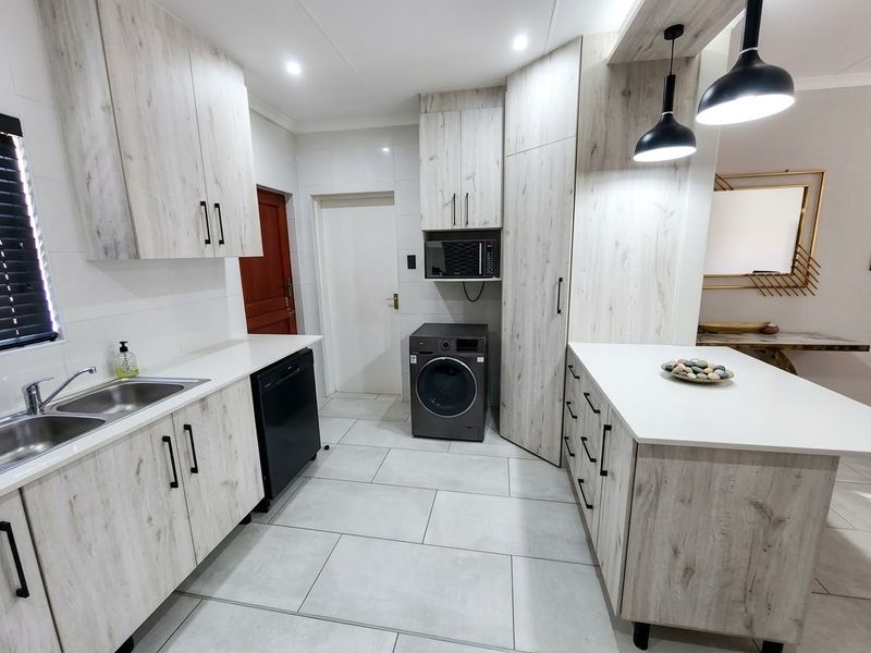 Modern kitchen featuring light wood-grain cabinetry, stone countertops, integrated microwave, and sleek pendant lighting with tiled flooring throughout.