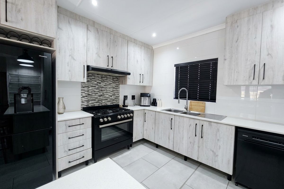 Modern kitchen featuring light wood-grain cabinetry, black appliances, gas hob, tiled backsplash, and sleek countertops in a well-maintained, contemporary space.