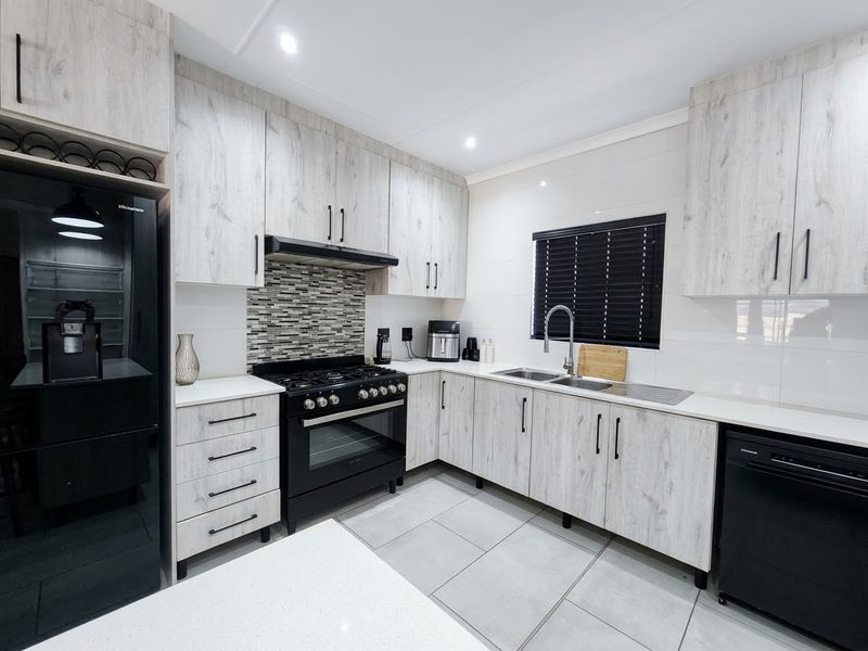 Modern kitchen featuring light wood-grain cabinetry, black appliances, gas hob, tiled backsplash, and sleek countertops in a well-maintained, contemporary space.