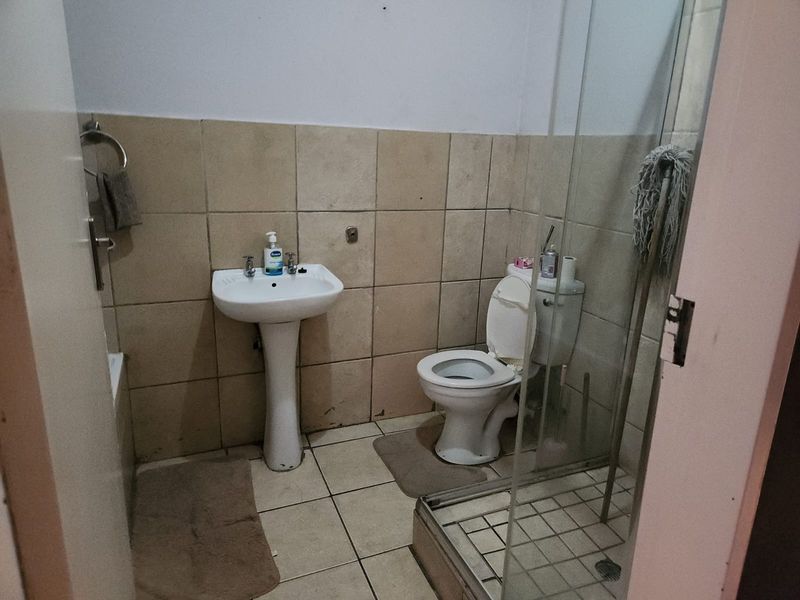 A functional bathroom featuring a pedestal basin, toilet, and a glass-enclosed shower with tiled finishes throughout.