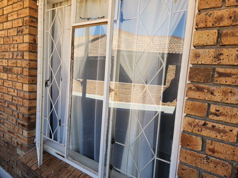 Close-up view of a face brick exterior wall featuring a window with a security gate showing signs of wear and peeling paint.