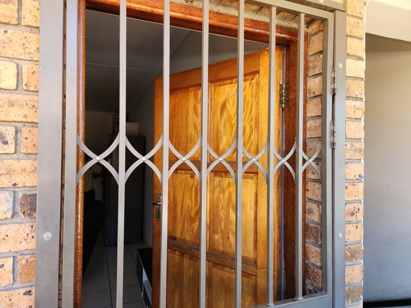 Entrance view featuring a sturdy metal security gate and a solid timber door set within a face brick exterior wall.