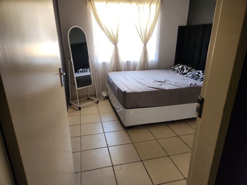 A functional bedroom featuring tiled flooring and natural light through a window with curtain rails.