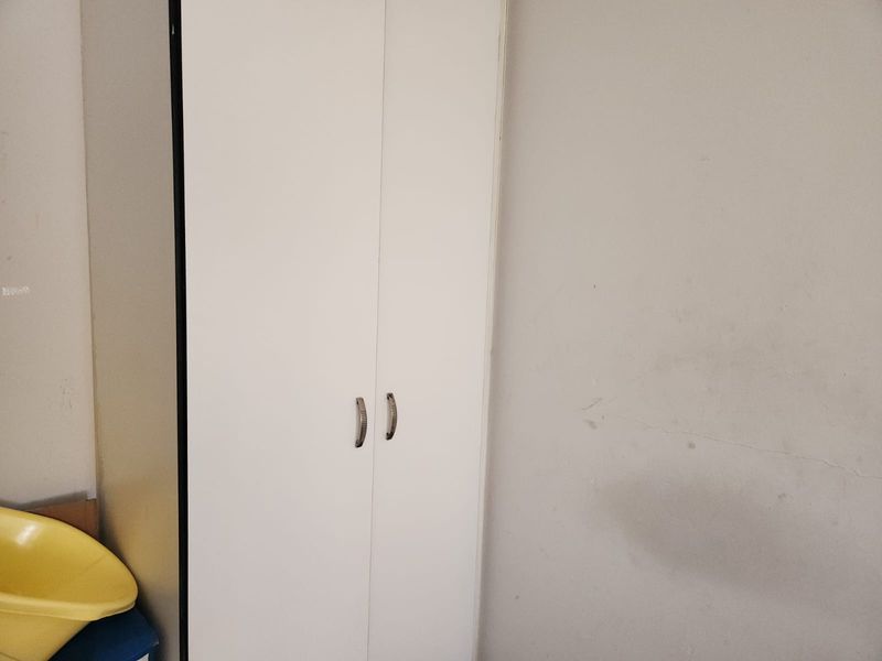 A bedroom interior featuring a white built-in wardrobe with metal handles against a plain wall.