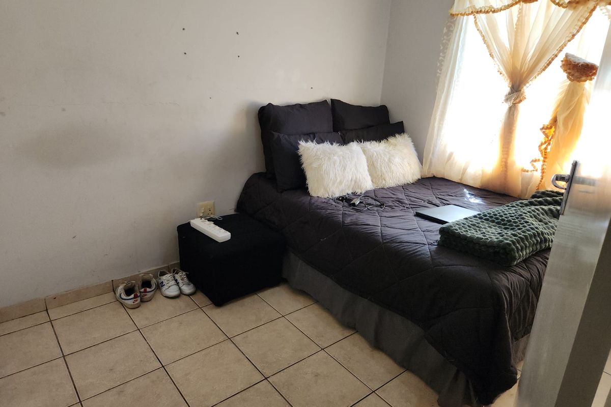 A compact bedroom featuring tiled flooring and a window with natural light, requiring minor cosmetic updates to the wall finishes.