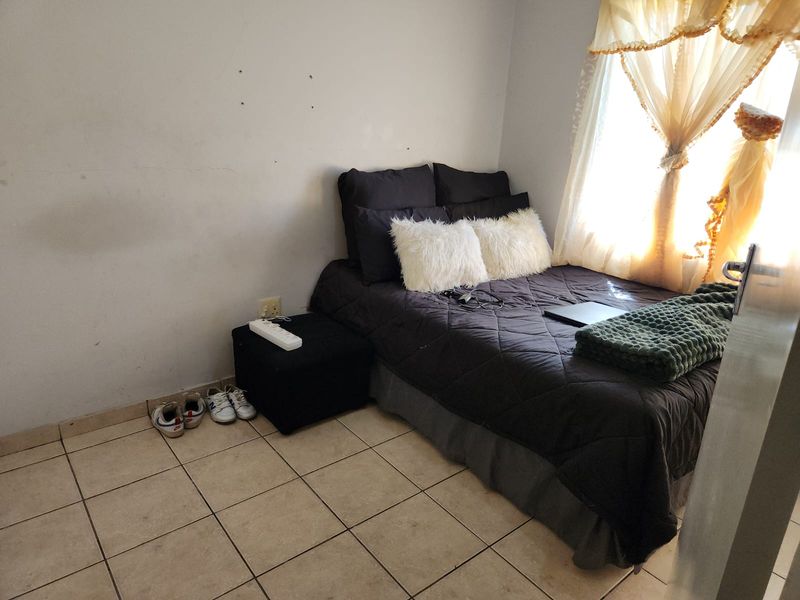 A compact bedroom featuring tiled flooring and a window with natural light, requiring minor cosmetic updates to the wall finishes.