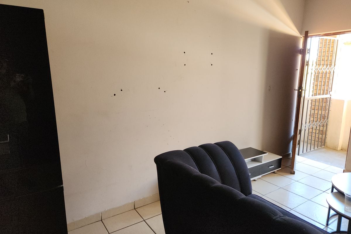 Living room area featuring tiled flooring and access to an exterior space through a security gate, with visible wall damage requiring repair.
