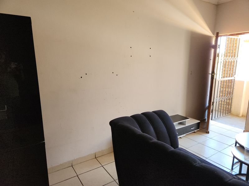 Living room area featuring tiled flooring and access to an exterior space through a security gate, with visible wall damage requiring repair.