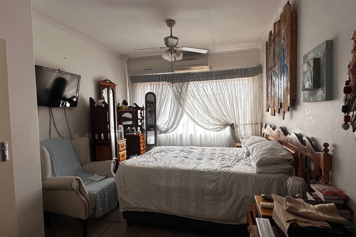 A bedroom featuring tiled flooring, a ceiling fan, and a wall-mounted air conditioning unit, providing a functional and comfortable living space.