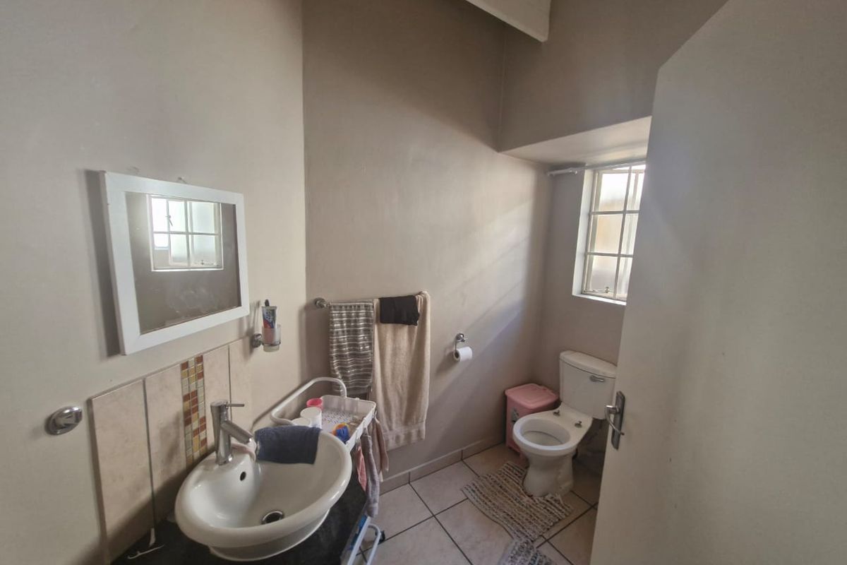 A functional bathroom featuring a pedestal basin, toilet, and tiled flooring with natural light from a small window.