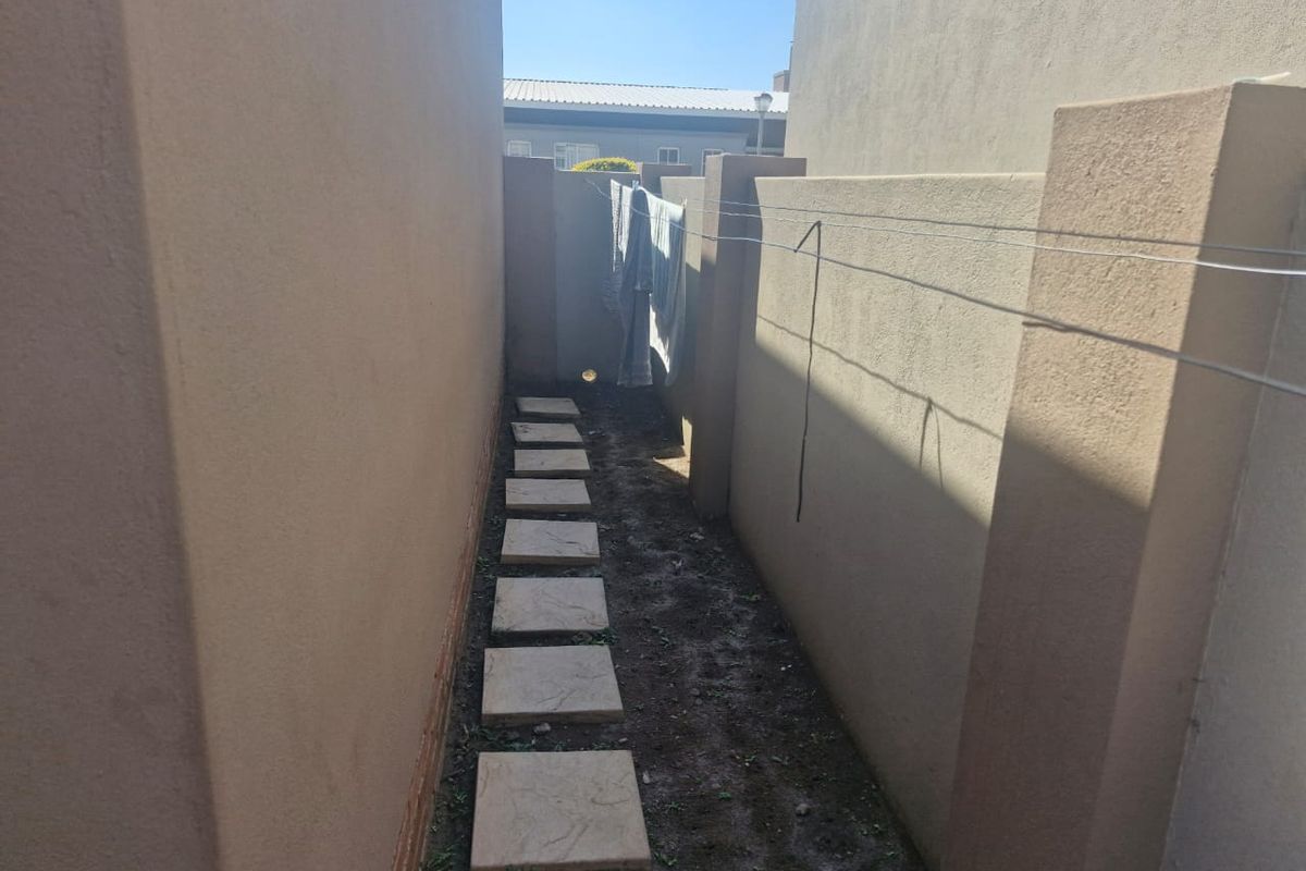 A narrow side passage featuring a paved stepping stone path and a fixed washing line between two boundary walls.
