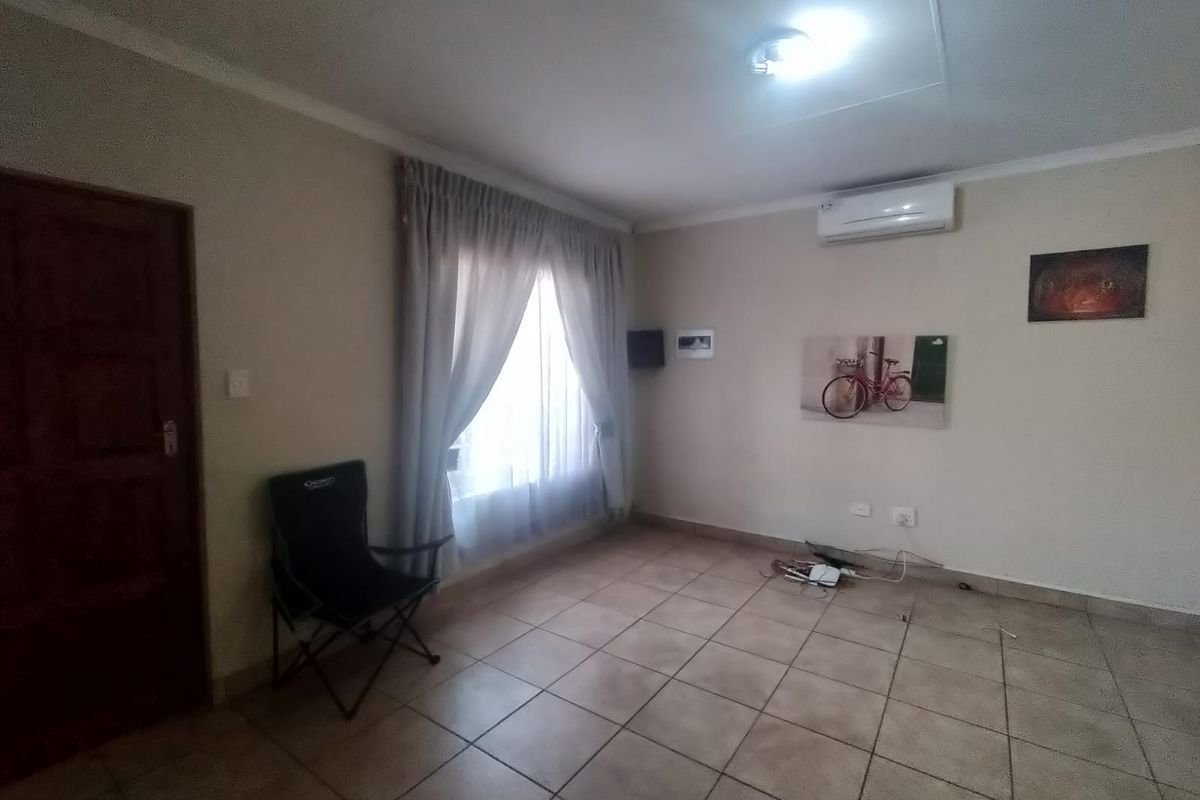A living room featuring tiled flooring, a wall-mounted air conditioning unit, and a wooden door, offering a functional and neutral living space.