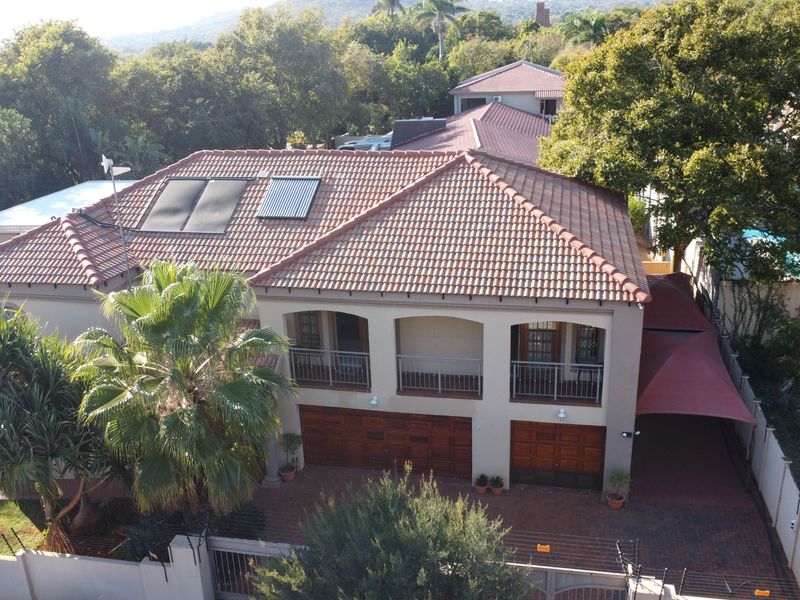 Aerial view of a residential property featuring a tiled roof with solar panels, double garage, balcony, and paved driveway within a landscaped setting.