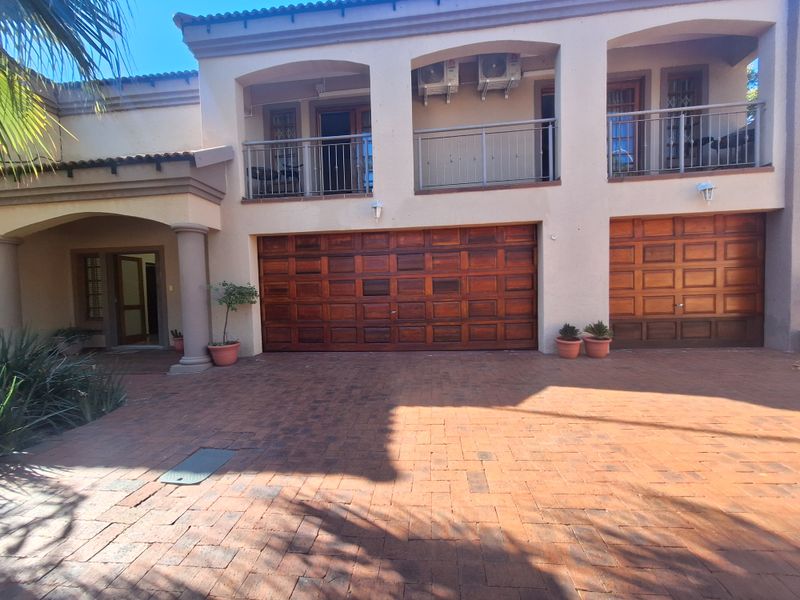 Front elevation of a multi-story house featuring a paved driveway, double and single wooden garage doors, and upper-level balconies with metal railings.